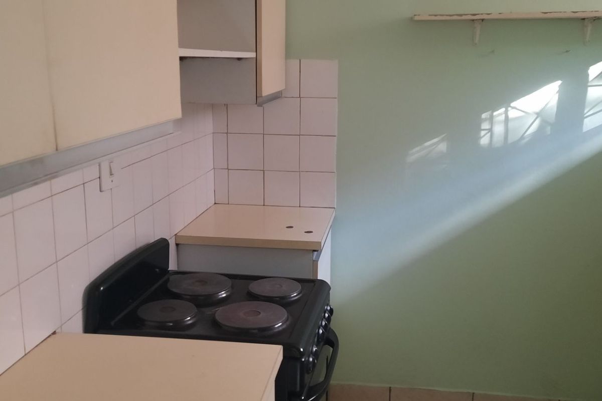 A compact, dated kitchen featuring built-in cabinetry, a tiled splashback, and an electric stove, offering potential for a modern renovation.