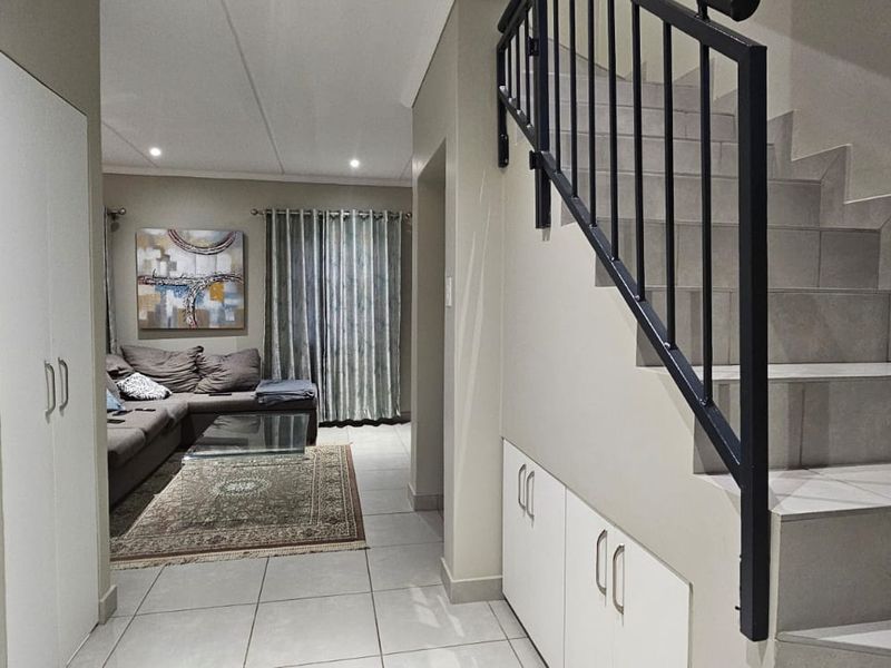 A well-maintained hallway featuring a tiled staircase with a metal balustrade, integrated under-stair storage, and a built-in cupboard, leading into the living area.
