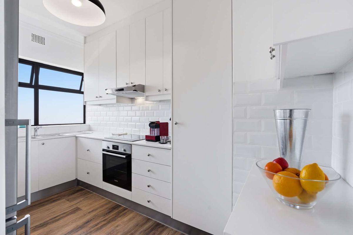 Modern, well-lit kitchen featuring white cabinetry, subway tile backsplash, integrated oven, electric cooktop, and a stainless steel sink with a view.