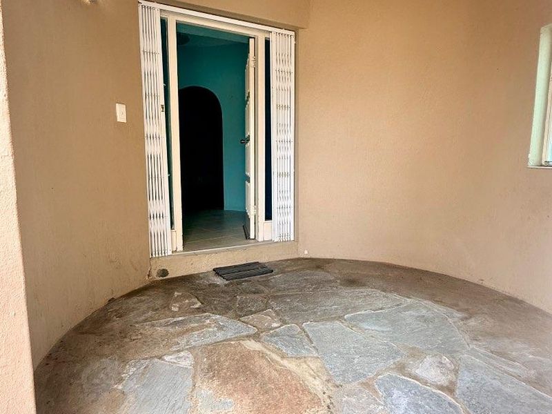 A covered entrance area featuring natural stone flagstone flooring and a security gate, providing a functional transition space into the home.