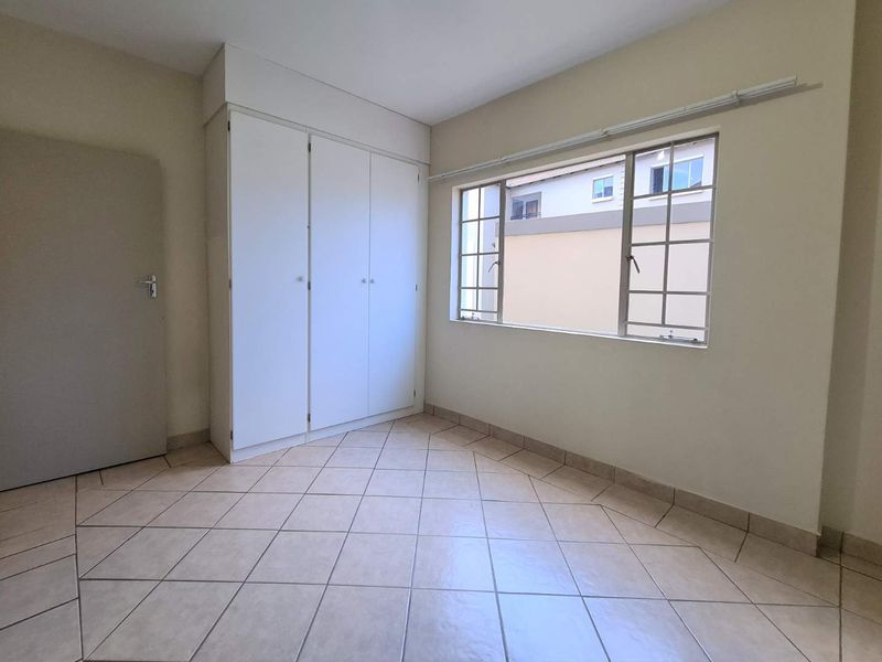 A clean, empty bedroom featuring neutral tiled flooring and built-in white cupboards, offering a blank canvas for personalization.