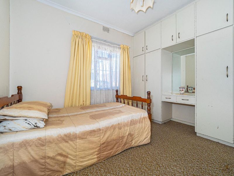 A bedroom featuring built-in cupboards with an integrated vanity unit and carpeted flooring, offering a dated aesthetic ready for modernization.