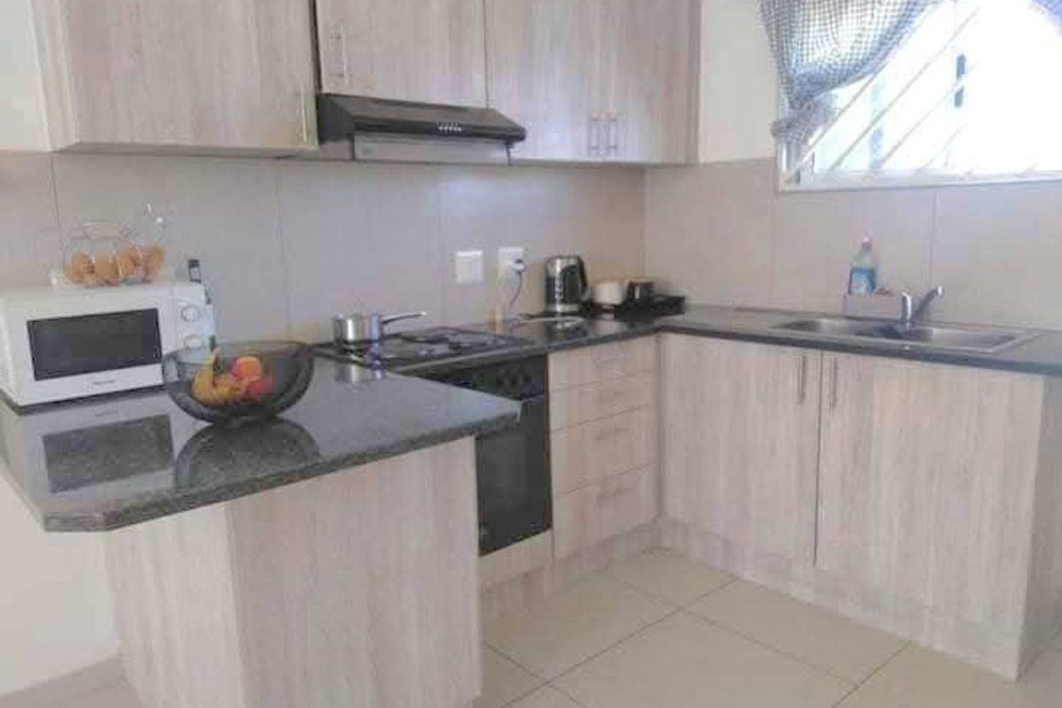 Functional kitchen featuring light wood-look laminate cabinetry, granite countertops, built-in oven with gas hob, and tiled flooring.