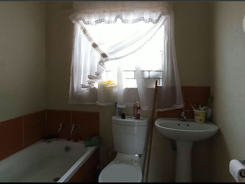 A functional bathroom featuring a bathtub, pedestal basin, and toilet with tiled splashbacks, requiring cosmetic updates to modernize the space.