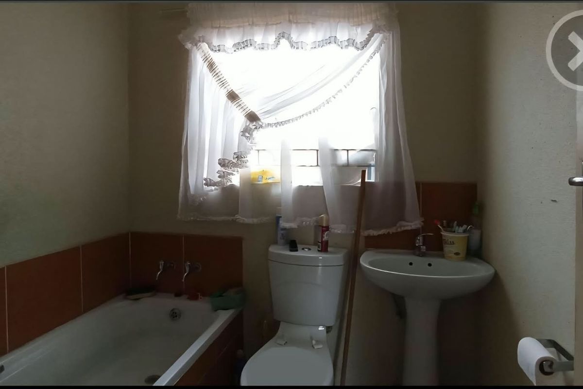 A functional bathroom featuring a bathtub, pedestal basin, and toilet with tiled splashbacks, requiring cosmetic updates to modernize the space.
