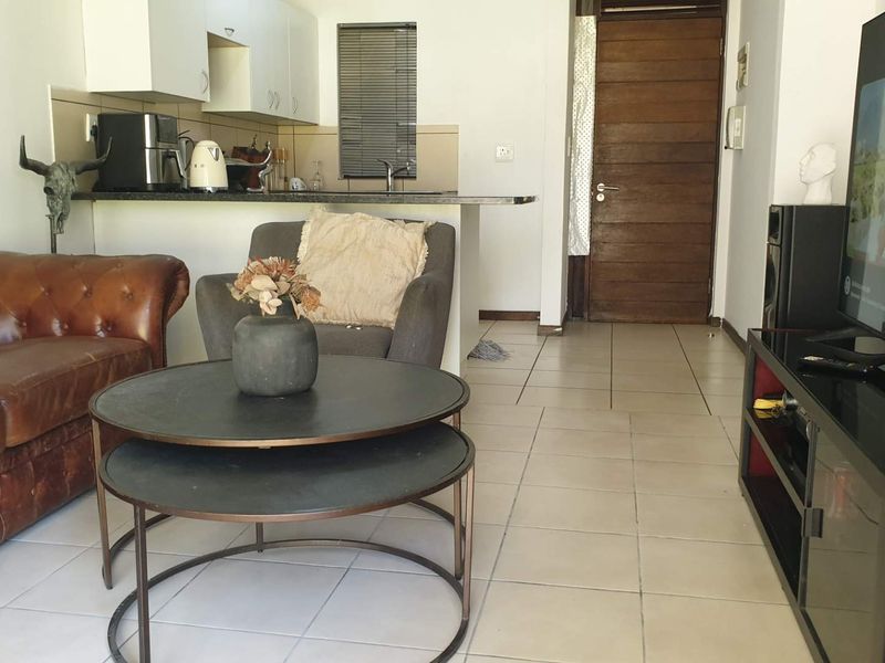Open plan living area featuring tiled flooring, a compact kitchen with built-in cabinetry, and a wooden entrance door.