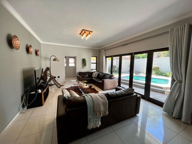Spacious living room featuring large sliding glass doors that open directly onto the pool area, complemented by modern tiled flooring and recessed lighting.