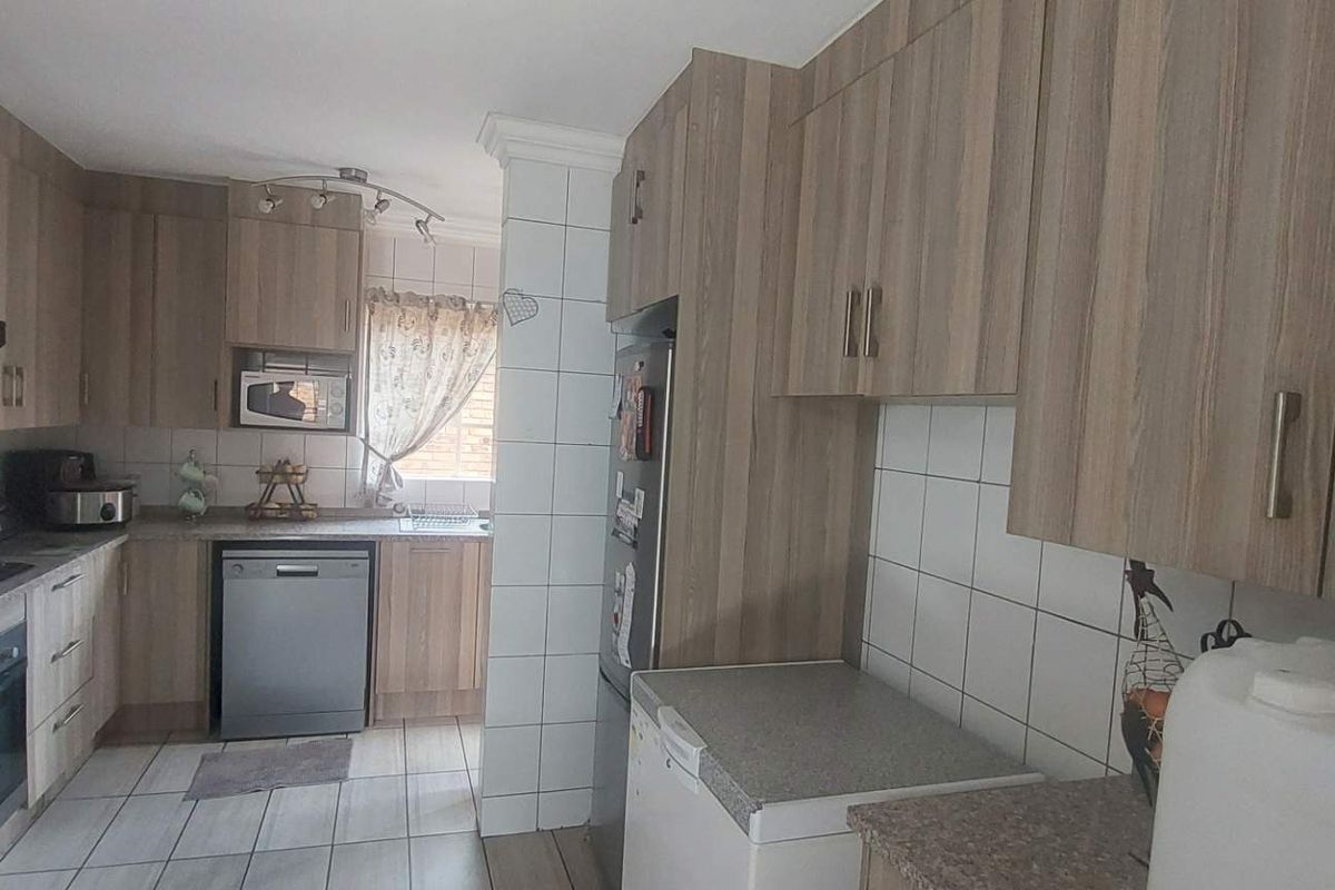 A functional kitchen featuring wood-look cabinetry, tiled splashbacks, built-in oven, hob, and extractor fan with tiled flooring throughout.