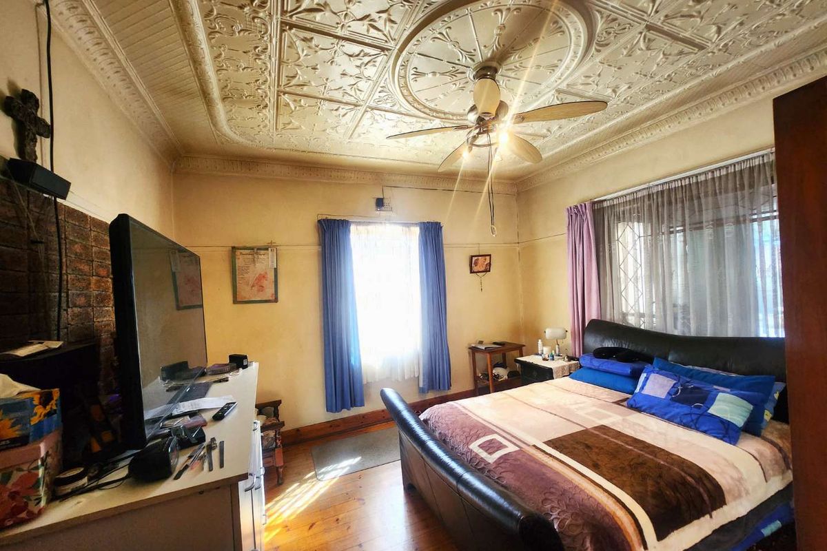 Spacious bedroom featuring a decorative pressed metal ceiling, ceiling fan, timber flooring, and a brick feature wall.