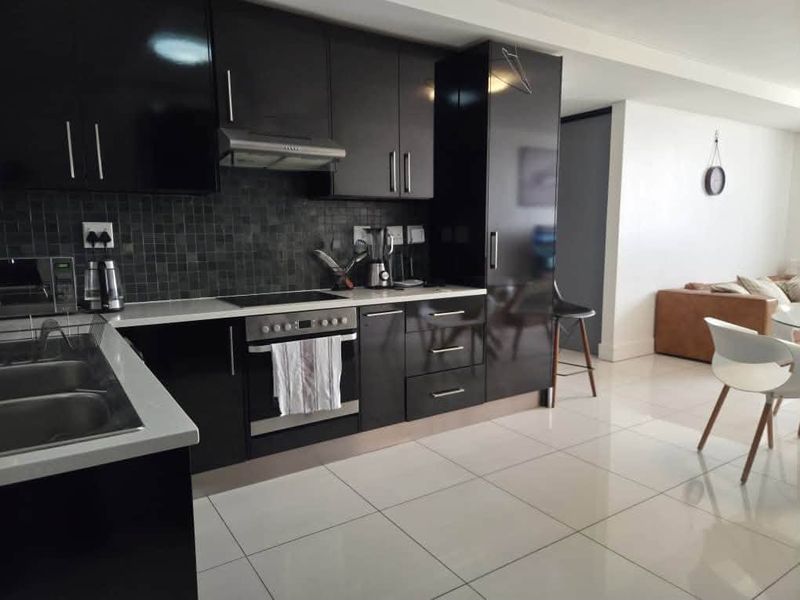 Modern open-plan kitchen featuring sleek black cabinetry, stone countertops, mosaic tile backsplash, and integrated appliances, flowing seamlessly into the adjacent living area.
