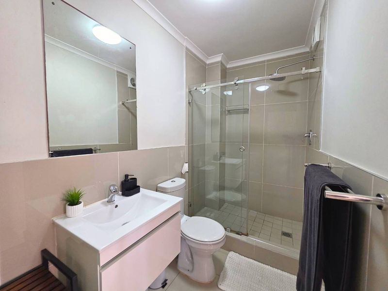 Modern bathroom featuring a vanity cabinet, wall-mounted mirror, toilet, and a glass-enclosed shower with tiled finishes.