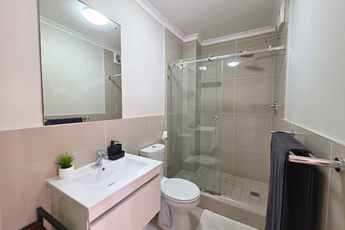 Modern bathroom featuring a vanity cabinet, wall-mounted mirror, toilet, and a glass-enclosed shower with tiled finishes.