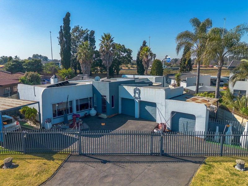 Aerial view of a residential property featuring a triple garage configuration, paved driveway, and secure metal perimeter fencing.