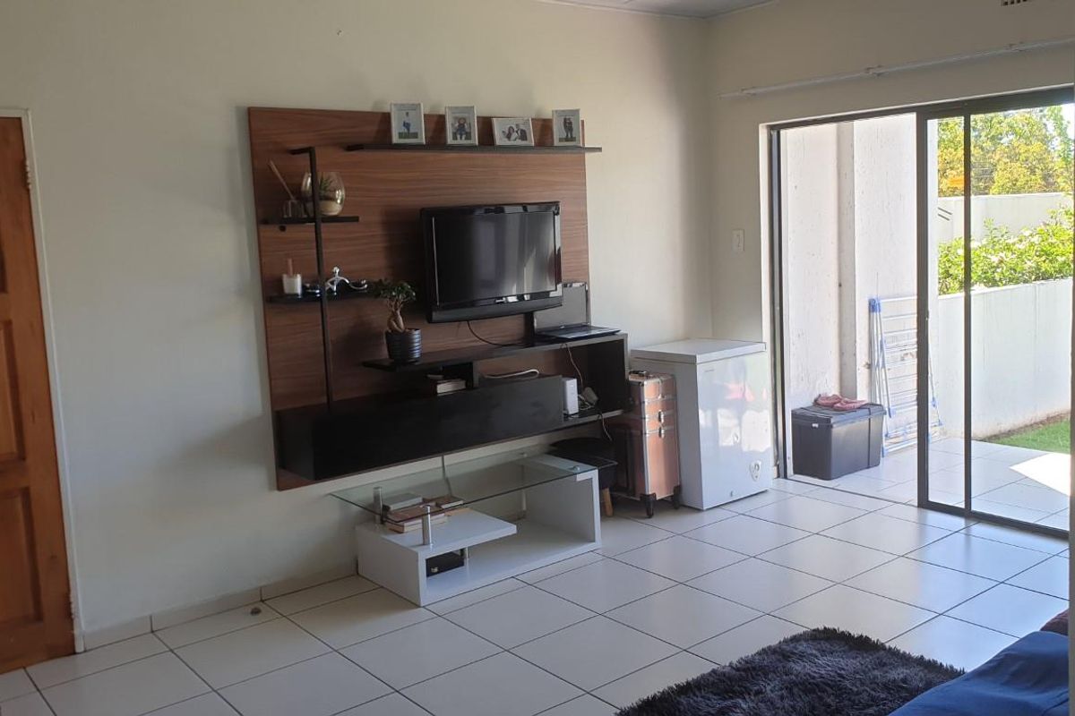 A living room featuring tiled flooring, a wall-mounted media unit, and sliding glass doors providing direct access to an outdoor patio area.