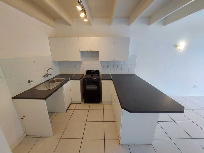 A functional kitchen featuring white cabinetry, dark laminate countertops, a freestanding stove, and tiled flooring with exposed ceiling beams.