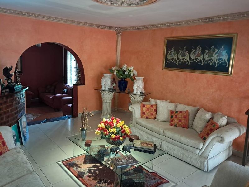 Spacious living room featuring an arched entryway, decorative ceiling rose, ornate crown molding, and a brick fireplace, finished with tiled flooring.