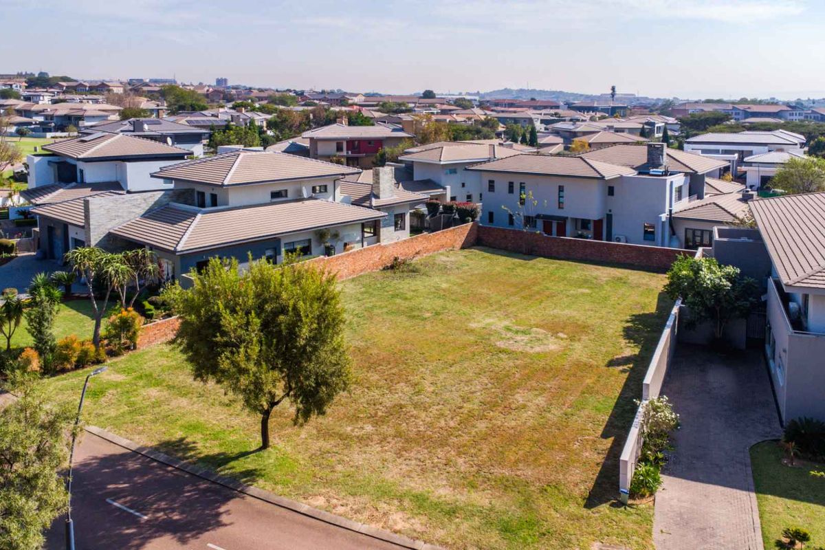 An elevated aerial view of a vacant residential plot situated within a developed suburban estate, surrounded by established modern homes.