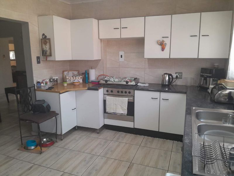 A functional kitchen featuring white built-in cabinetry, laminate countertops, a gas hob with oven, and tiled splashbacks with neutral floor tiles.