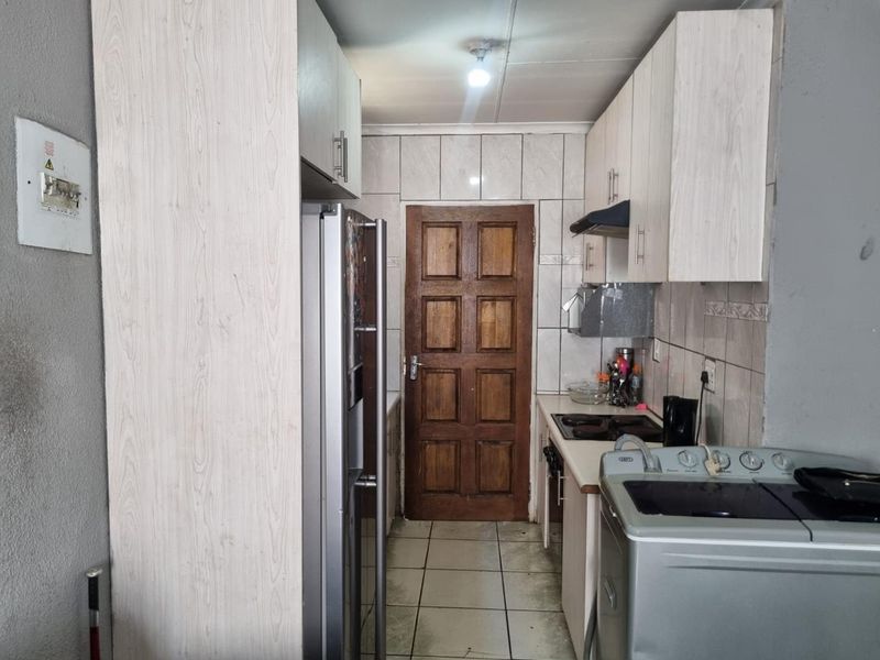 Compact kitchen featuring light wood-look cabinetry, tiled backsplash, and functional built-in cooking appliances with direct access to an adjacent room.