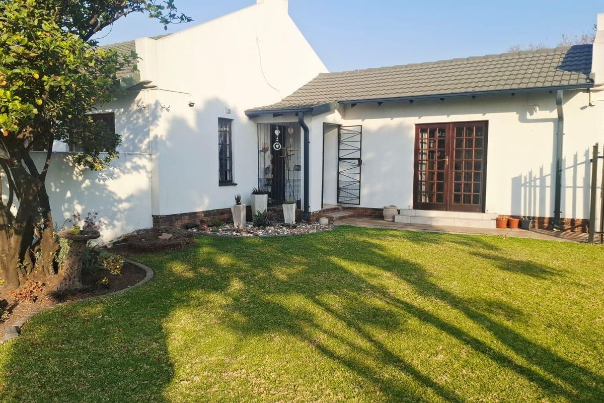 A well-maintained rear exterior view of the house featuring a landscaped garden, tiled roof, and secure access points with french doors.