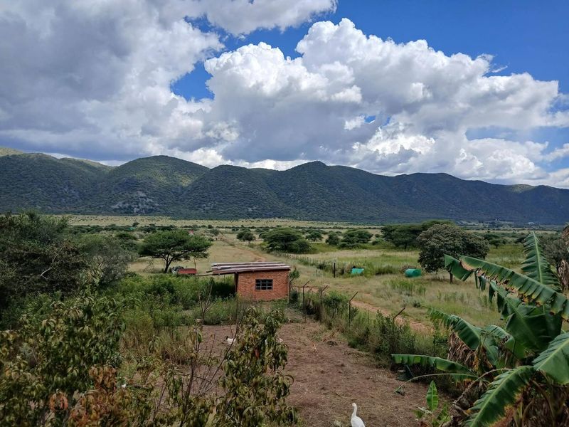 A scenic view of the expansive farm landscape featuring rolling mountains, natural vegetation, and a small brick outbuilding in the distance.