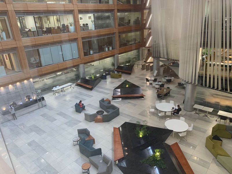 Spacious modern office atrium featuring a multi-level design, glass facade, stone flooring, and integrated planters in a professional corporate environment.