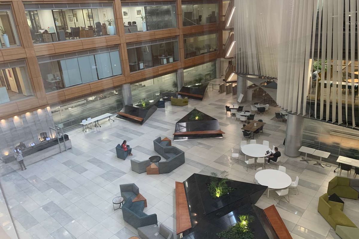 Spacious modern office atrium featuring a multi-level design, glass facade, stone flooring, and integrated planters in a professional corporate environment.