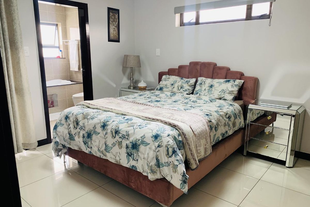 A well-maintained bedroom featuring tiled flooring, a high-level horizontal window, and an en-suite bathroom with a bathtub.