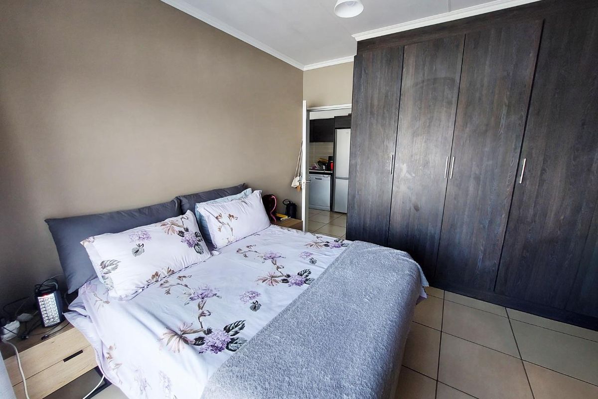 A bedroom featuring dark wood built-in cupboards and tiled flooring, with a view into the adjacent kitchen area.
