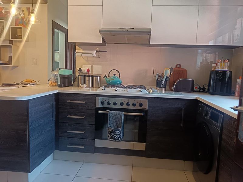 Modern kitchen featuring dark wood-grain cabinetry, white upper cabinets, stone countertops, a gas hob, and an integrated oven with a sleek extractor fan.