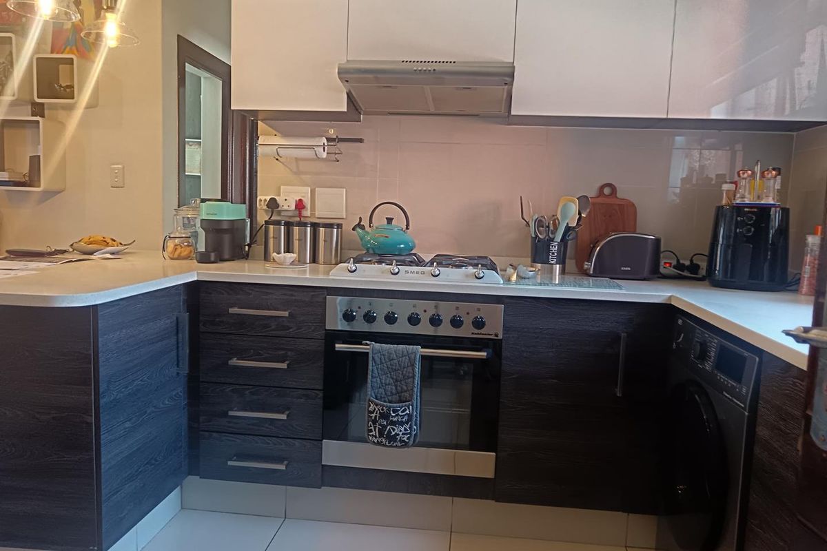 Modern kitchen featuring dark wood-grain cabinetry, white upper cabinets, stone countertops, a gas hob, and an integrated oven with a sleek extractor fan.