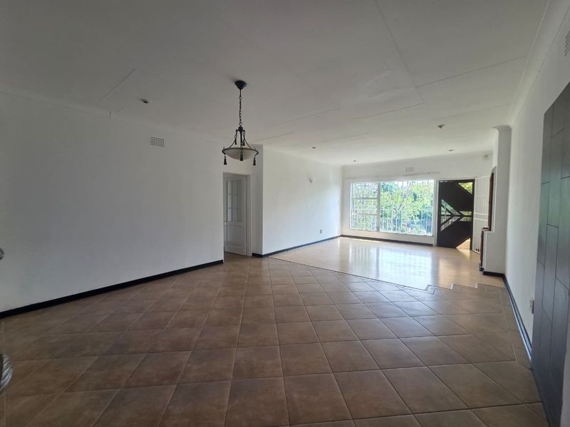 Spacious, open-plan living area featuring a combination of tiled and laminate flooring, large windows with security bars, and direct access to the entrance.