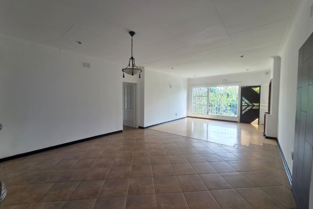 Spacious, open-plan living area featuring a combination of tiled and laminate flooring, large windows with security bars, and direct access to the entrance.