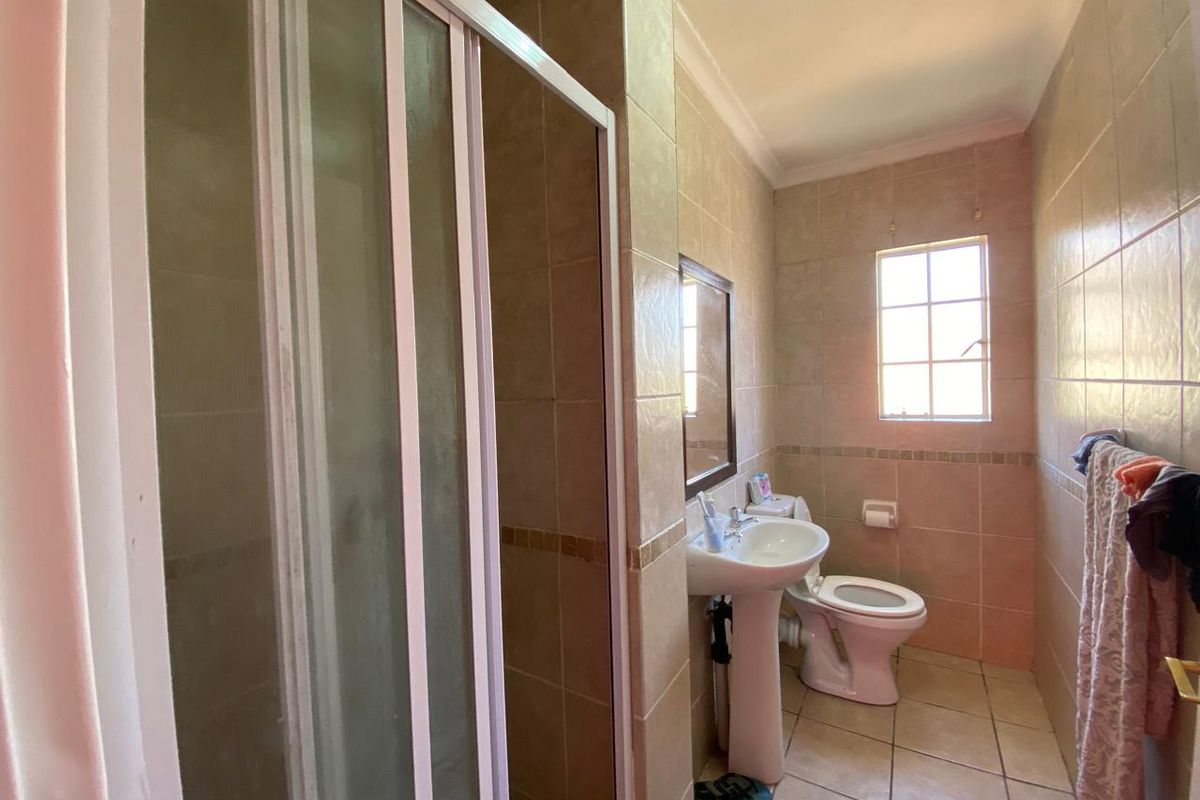 A functional bathroom featuring a shower enclosure, pedestal basin, and toilet with neutral wall and floor tiling.