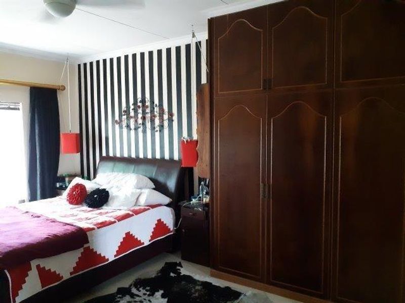 A bedroom featuring dark wood built-in cupboards and a ceiling fan, with a striped feature wall.