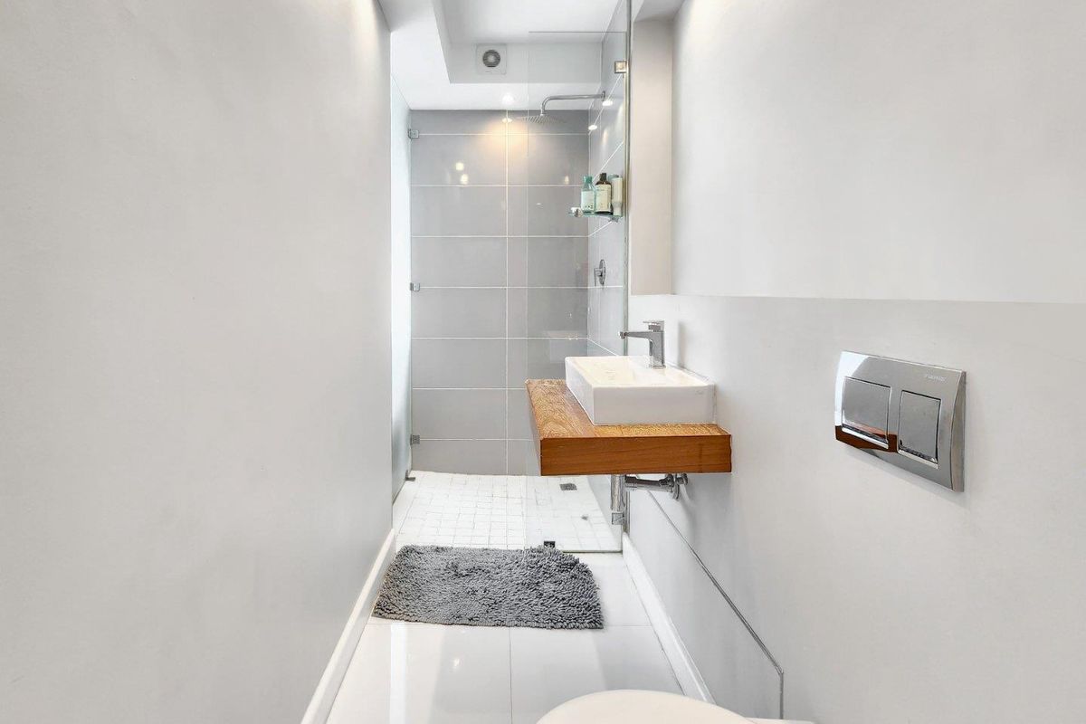 Modern bathroom featuring a walk-in shower with glass screen, wall-mounted timber vanity with vessel sink, and a concealed cistern toilet.