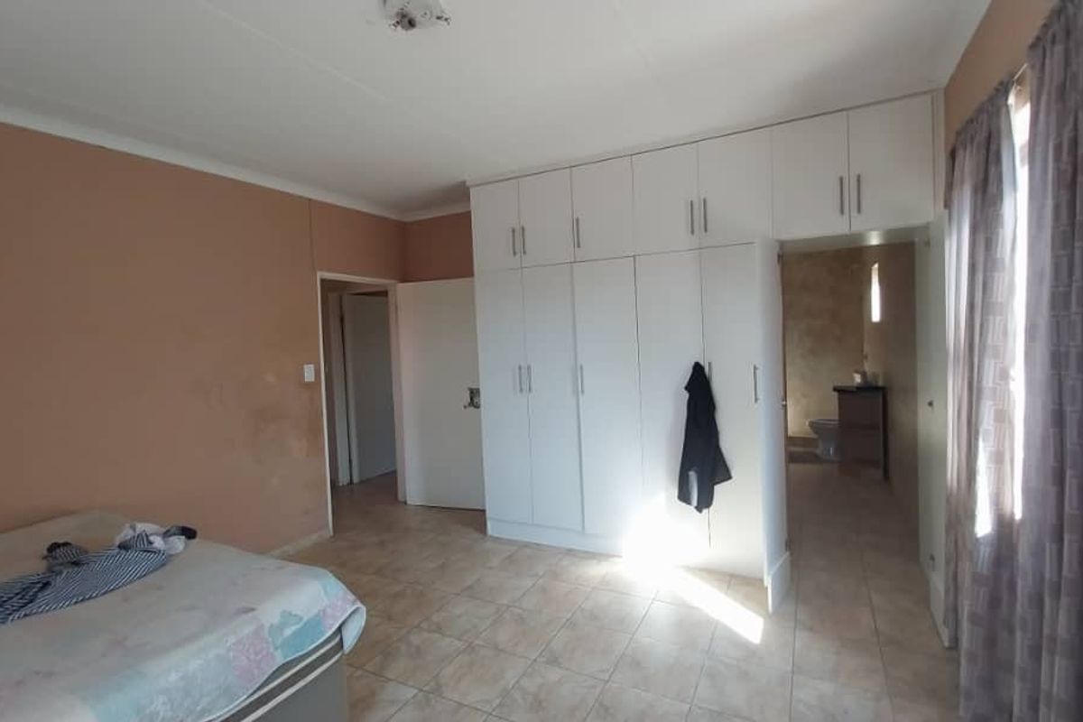 A bedroom featuring built-in white cabinetry, tiled flooring, and an adjoining en-suite bathroom area.