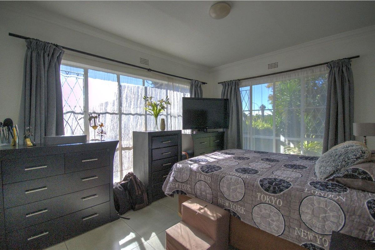 A bright bedroom featuring large windows with natural light, tiled flooring, and crown molding, offering a comfortable and airy living space.
