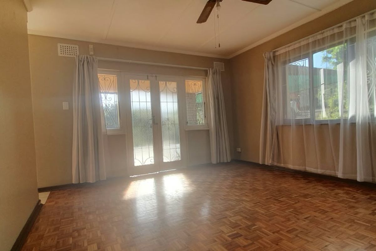 Spacious living room featuring classic parquet flooring, a ceiling fan, and direct access to the exterior through secure french doors.