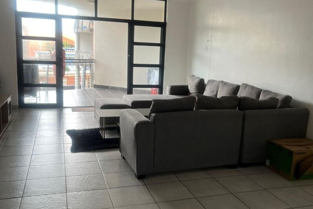 Spacious living area featuring neutral tiled flooring and large aluminium-framed glass doors providing access to an outdoor balcony.