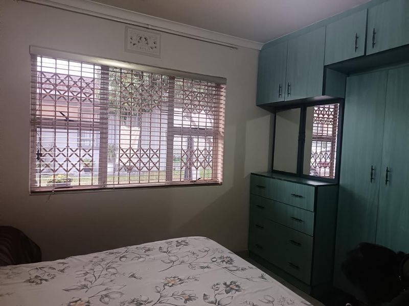 A bedroom featuring built-in cupboards with integrated vanity and a window fitted with security bars and venetian blinds.