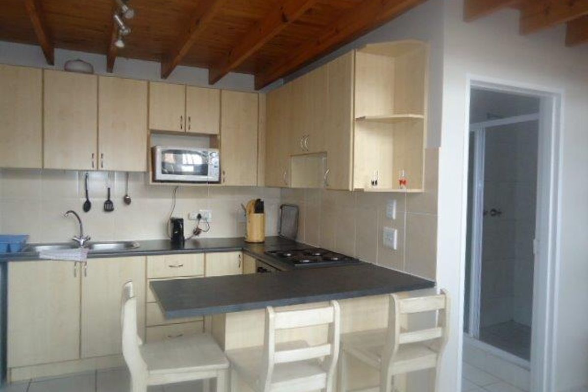 Functional kitchen featuring light wood cabinetry, laminate countertops, built-in appliances, and a breakfast bar, set beneath an exposed timber beam ceiling.