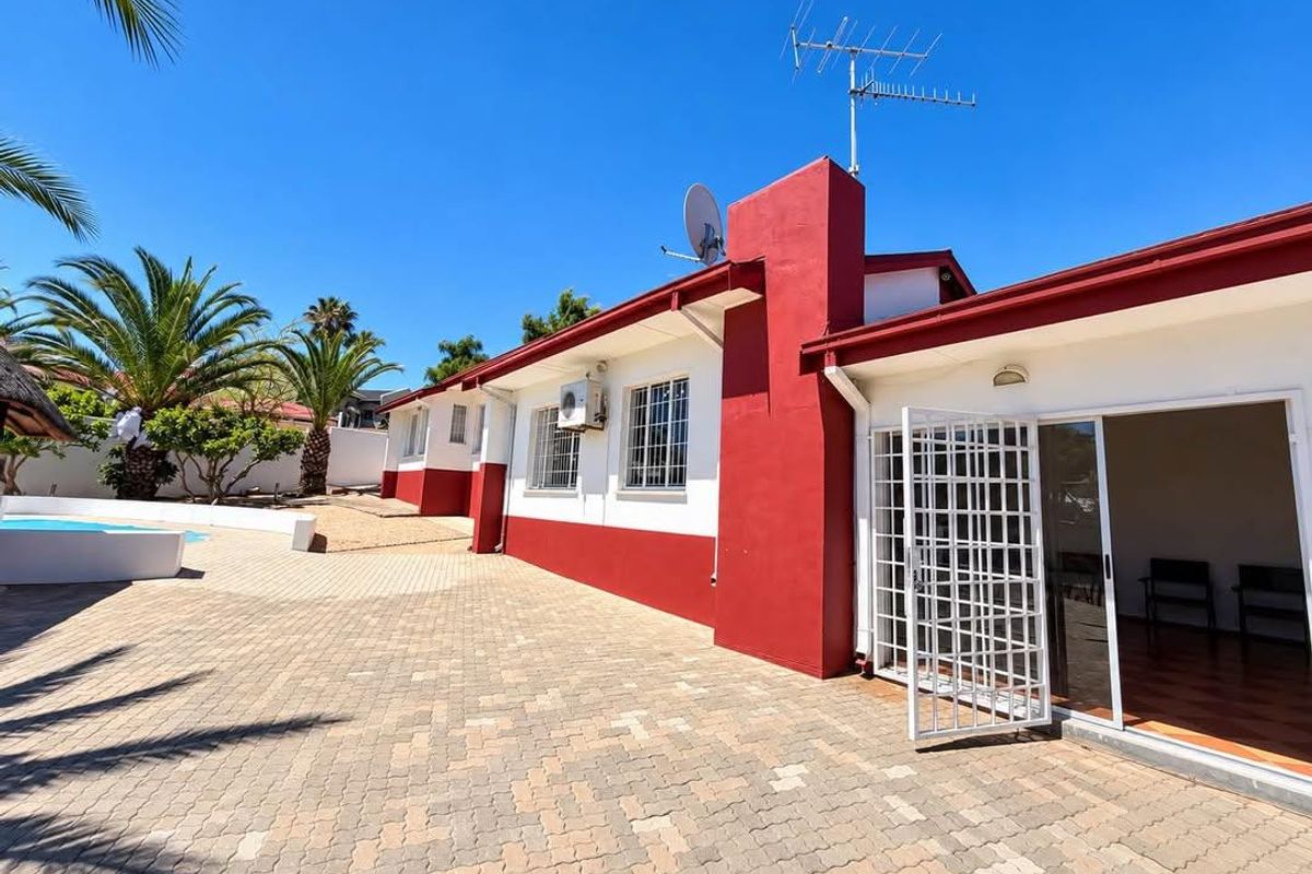 Rear exterior view featuring a paved patio area, swimming pool, and access to the home via a sliding glass door with security gate.
