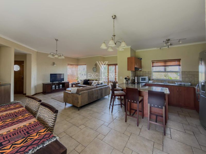 Spacious open-plan living area featuring a functional kitchen with granite countertops, a central island, and tiled flooring throughout the combined dining and lounge space.