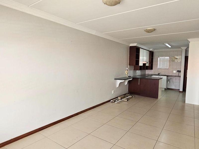 An open-plan living and kitchen area featuring tiled flooring, built-in cabinetry, and a breakfast bar, offering a functional blank canvas for renovation.