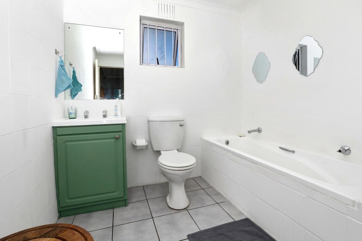 A functional bathroom featuring a white bathtub, a toilet, and a green vanity cabinet with a wall-mounted mirror.