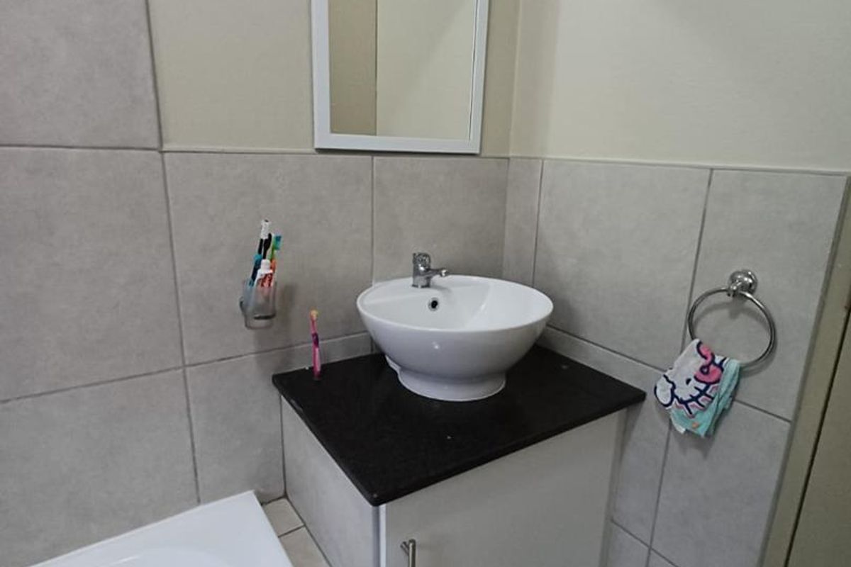 A clean bathroom featuring a vessel sink on a granite vanity, tiled walls, and a bathtub.
