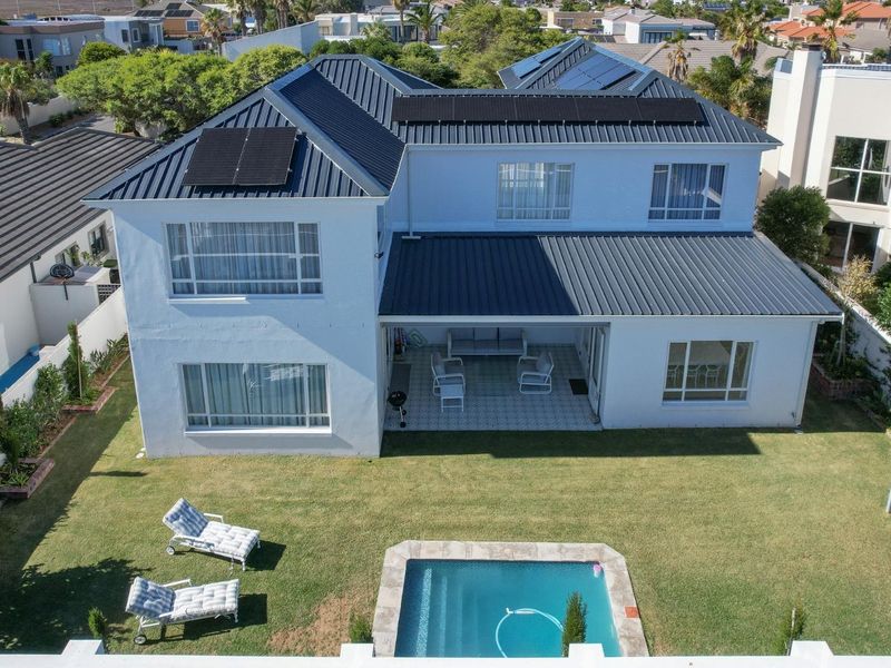 Aerial view of a two-story house featuring a metal roof with solar panels, a covered patio, a swimming pool, and a well-maintained garden.