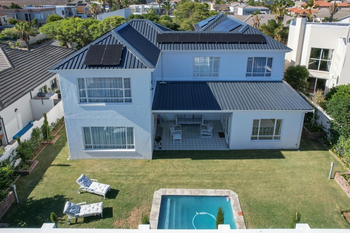 Aerial view of a two-story house featuring a metal roof with solar panels, a covered patio, a swimming pool, and a well-maintained garden.