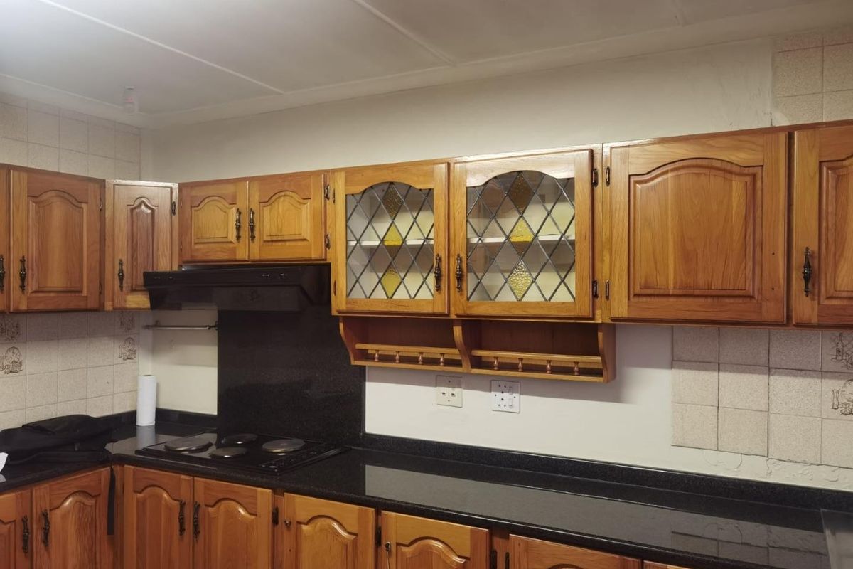 A functional kitchen featuring traditional wooden cabinetry, black granite countertops, a built-in hob, and an extractor fan with decorative leaded glass cabinet inserts.
